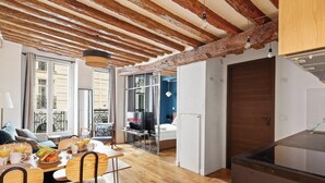 Un appartement moderne avec des poutres apparentes, un coin repas où le petit-déjeuner est servi, une télévision et une cuisine dotée d’un grand îlot central.
