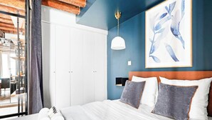 A bedroom with a bed, white wardrobe, blue walls, and a framed artwork. - Loft de charme avec verriere & poutre authentiques (Paris)