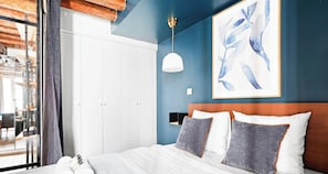 Un dormitorio con cama, armario blanco, paredes azules y una obra de arte enmarcada.