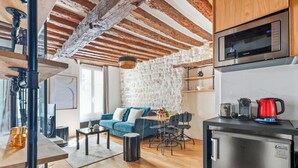 A modern kitchen with a microwave, a refrigerator, and a coffee maker. There is a dining area with a table and chairs, and a living room with a sofa and a coffee table. - Loft de charme avec verriere & poutre authentiques (Paris)