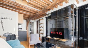 Un espacio moderno para vivir con techo de madera, zona de comedor con mesa y sillas, área de cocina y un amplio ventanal con el logotipo de Netflix.