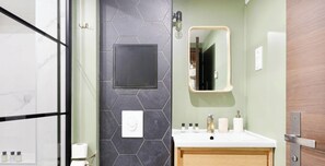A bathroom with a marble wall, a black hexagonal tile wall, a white sink, and a wooden vanity. - Loft de charme avec verriere & poutre authentiques (Paris)