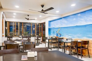 A restaurant with multiple tables and chairs, ceiling fans, and a large mural of a boat on water.
