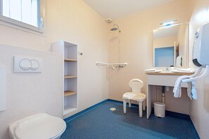 A bathroom with a toilet, a shower, a sink with a mirror, and a small chair. - Accessible Apartment With Terrace for 3 (Saumur)