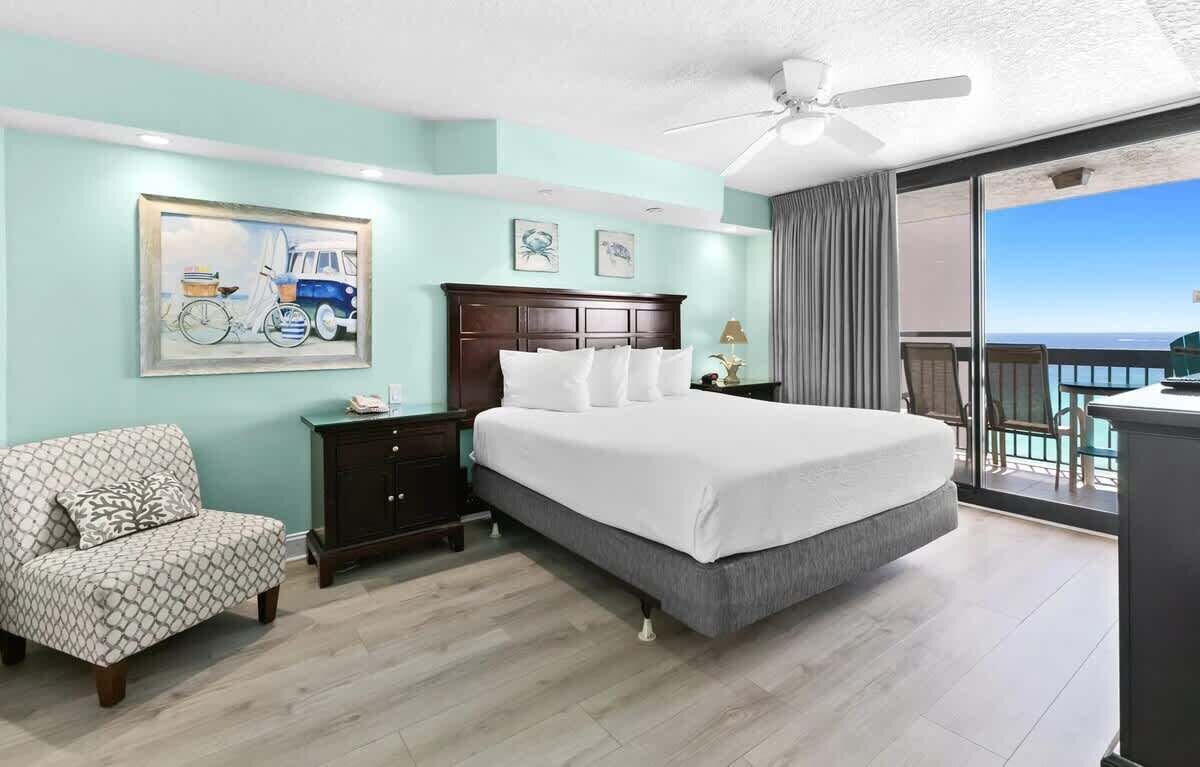 Een slaapkamer met een bed, een stoel, een nachtkastje, een plafondventilator en uitzicht op de oceaan.