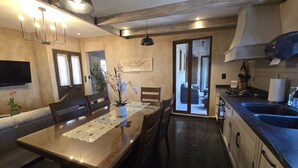 Zona pranzo con tavolo, sedie, una pianta in vaso e cucina con lavello e fornello.