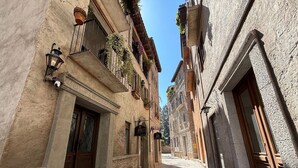 Una stretta strada acciottolata fiancheggiata da edifici storici con balconi, porte in legno e ringhiere in ferro battuto.
