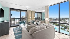 En rummelig stue med en stor sofa, et sofabord og et fjernsyn. Der er en balkon med udsigt over byen.