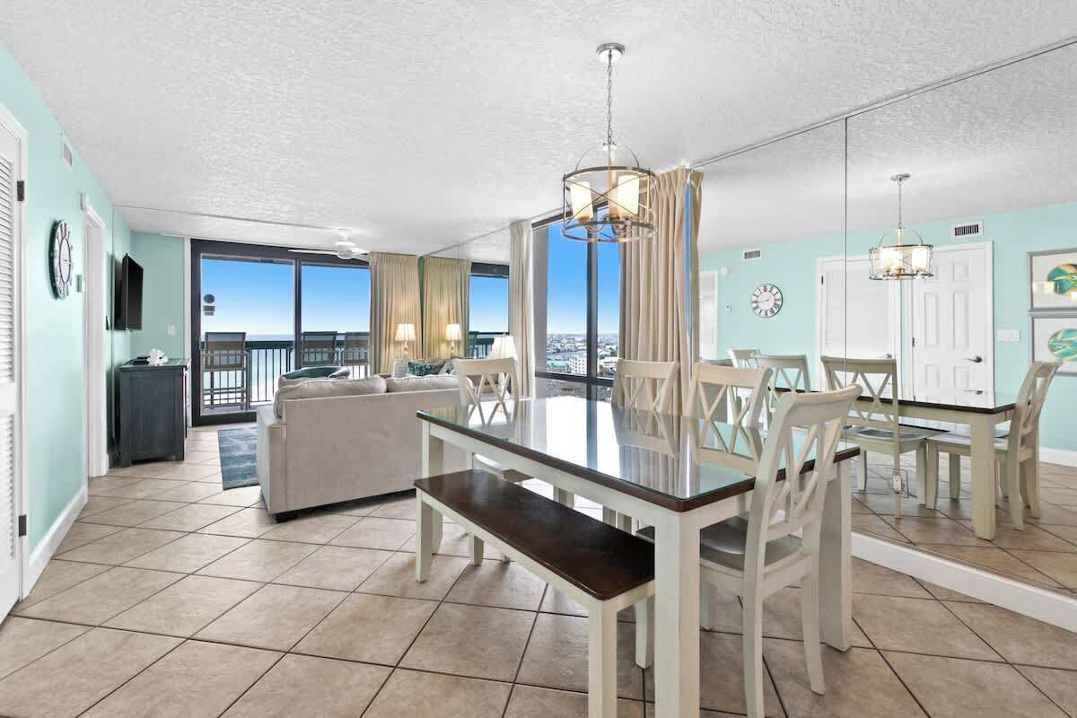 Un vaste espace de vie comprenant une table à manger avec un plateau en verre, des chaises blanches, un canapé et un balcon offrant une vue agréable.