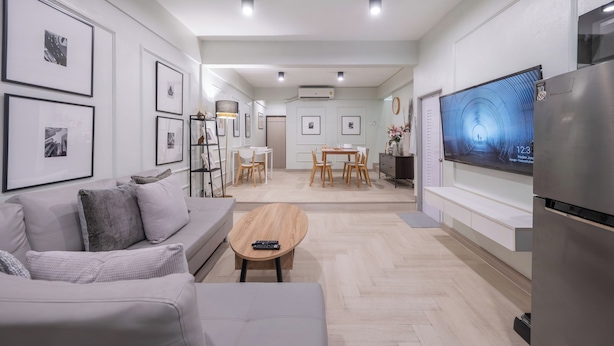 A modern living room with a sofa, coffee table, and TV. There is a dining area with chairs and a table in the background. - Arun Sa Wad House Lad phrao 6 Guests (Bangkok)