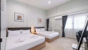 A hotel room with two beds, a desk, a chair, a radiator, and a window with curtains. - Arun Sa Wad House Lad phrao 6 Guests (Bangkok)
