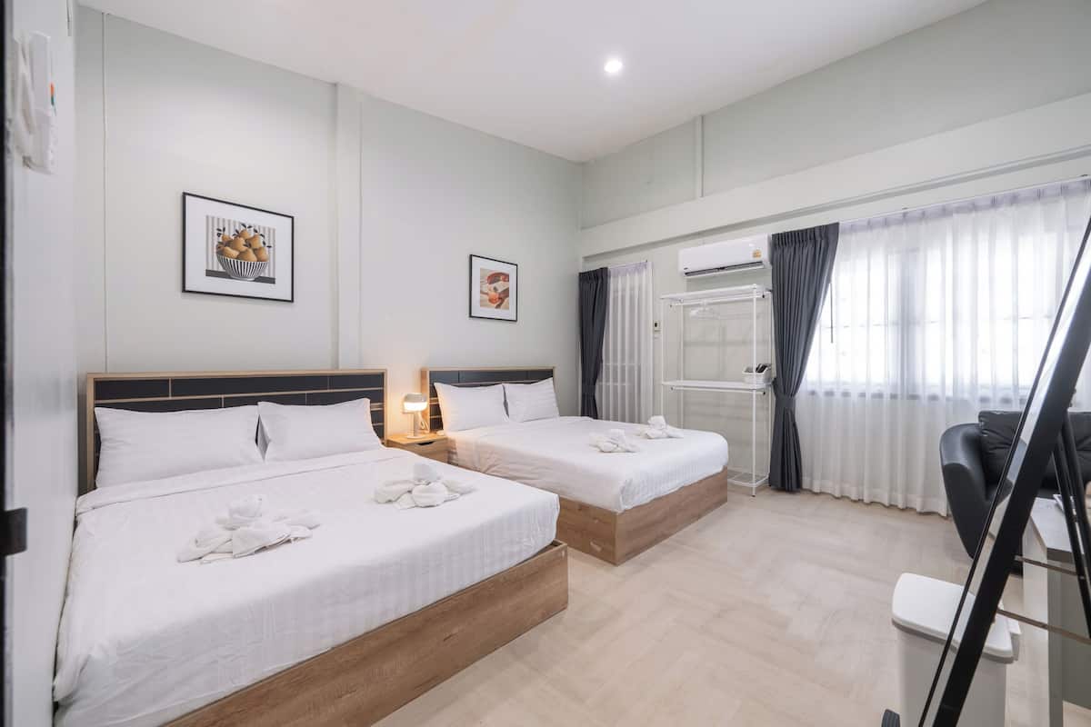 A hotel room with two beds, a desk, a chair, a radiator, and a window with curtains.