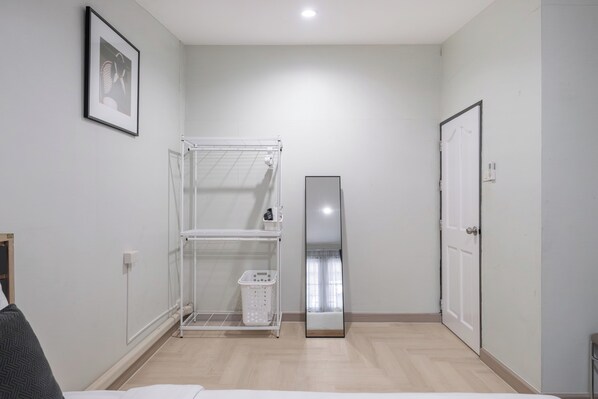 Une pièce avec un lit, un étendoir à linge blanc, une porte et un miroir.