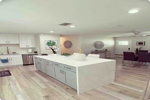 A modern kitchen with white cabinets, a central island, and a dining area with a table and chairs. - Spacious Tampa Retreat  Perfect for Groups + Prime Location (Tampa)
