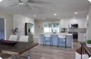 A modern kitchen with white cabinets, a central island with bar stools, a ceiling fan, and a large window. - Spacious Tampa Retreat  Perfect for Groups + Prime Location (Tampa)