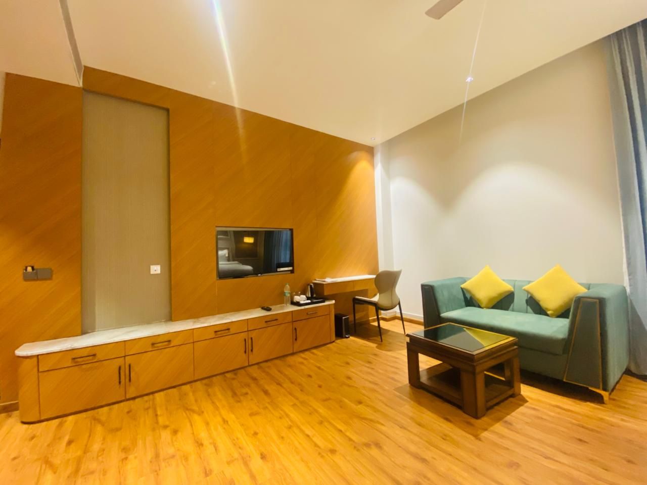 Un salon moderne avec un plancher en bois, un canapé agrémenté de coussins jaunes, une table basse et un téléviseur à écran plat fixé au mur.