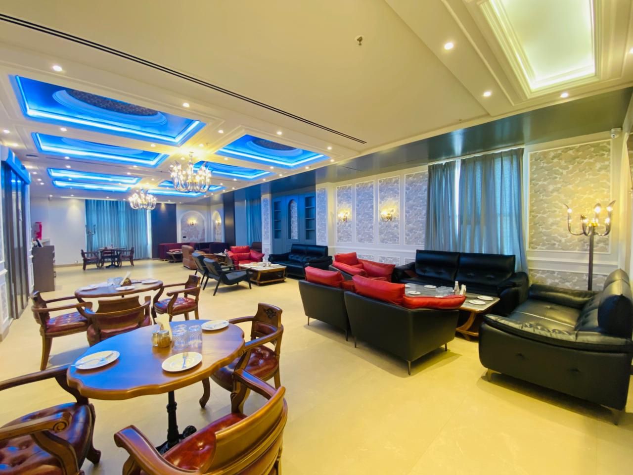 A spacious hotel lobby with a dining area, sofas, and a chandelier.
