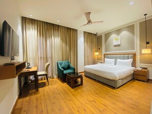 Ein Hotelzimmer mit einem Bett, einem Schreibtisch, einem Stuhl, einem Fernseher und einem Deckenventilator.