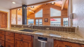 A kitchen with granite countertops, a dishwasher, wooden cabinets, and large windows overlooking a lake.