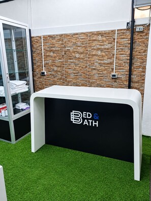 Una recepción con un logotipo, una vitrina de vidrio con toallas dobladas y una pared con textura de piedra.