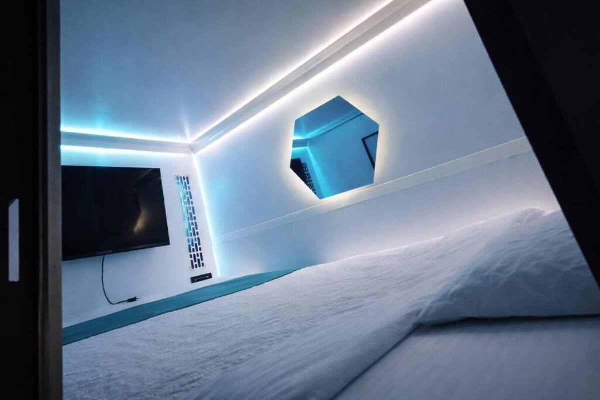 A modern bedroom with a flat-screen TV, a geometric light fixture, and a neatly made bed.