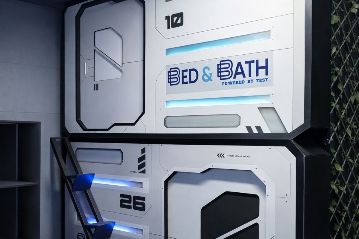 Una habitación moderna de diseño geométrico con una cama y un área de escritorio, identificada como 'BED & BATH' operado por TEST.