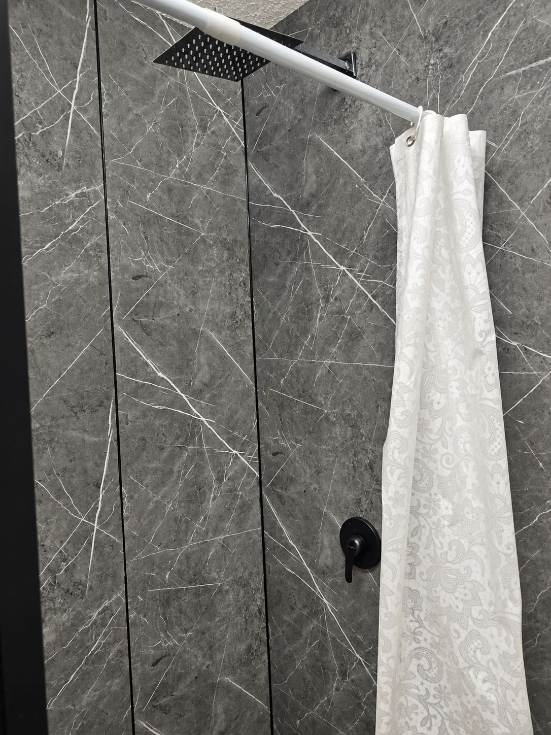 Un baño con cortina de ducha, cabezal de ducha y pared de mármol.