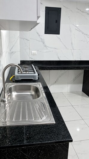 Una cocina con un lavamanos de acero inoxidable, una encimera negra y baldosas de mármol blanco.