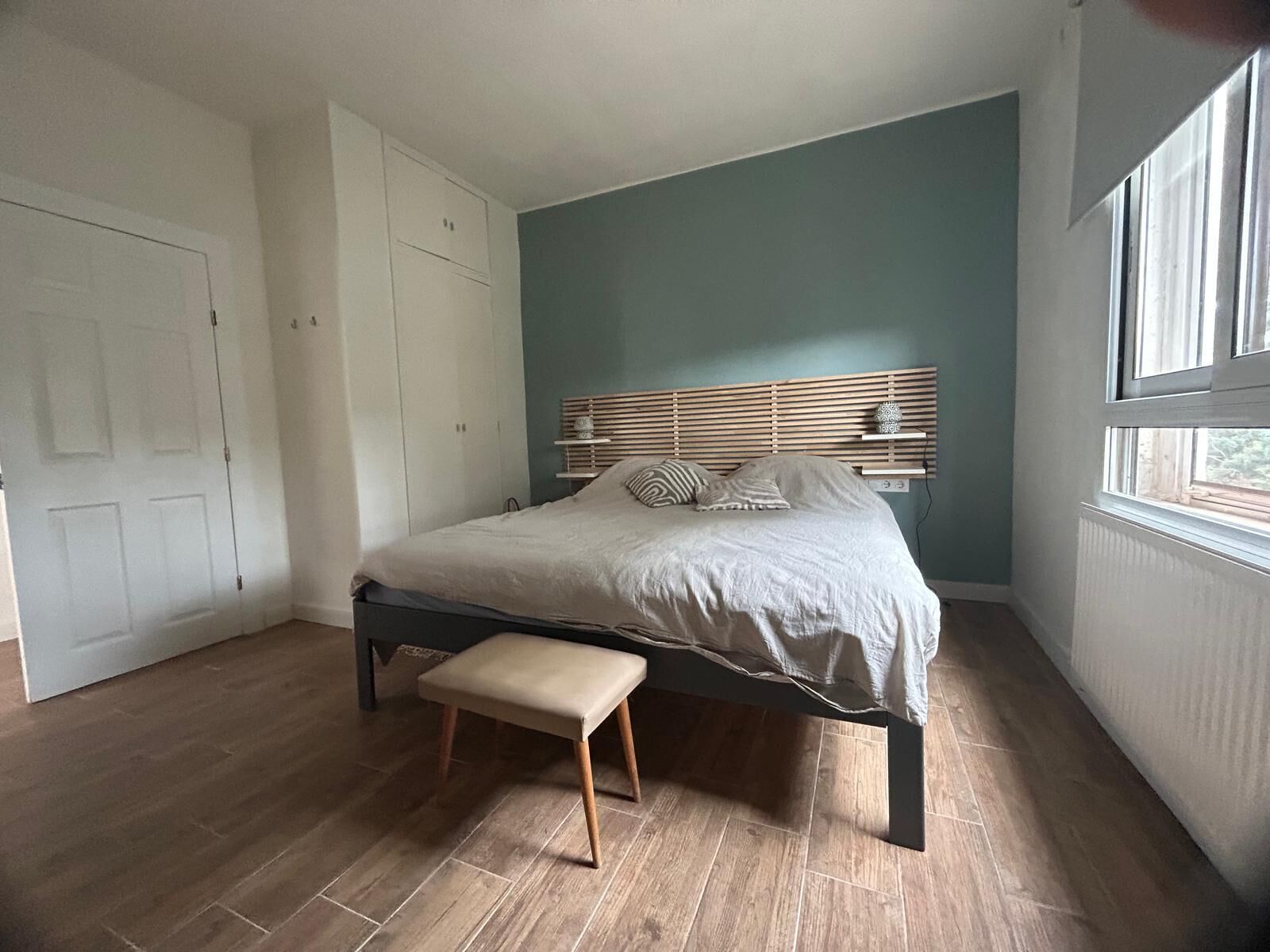 A bedroom with a bed, bench, wardrobe, and a window.