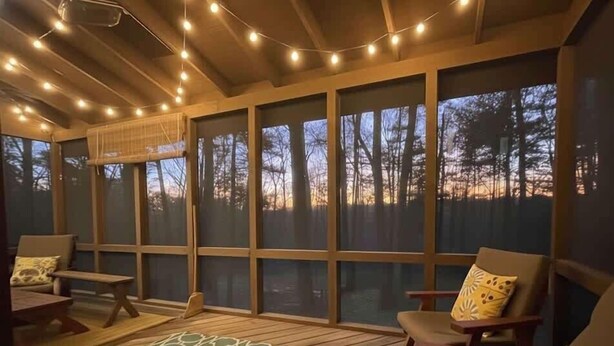 Une pièce confortable avec une grande fenêtre, un canapé et un fauteuil, offrant une vue sur les arbres à l’extérieur.