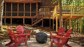 Une terrasse en bois, dotée de chaises Adirondack et d’un barbecue, entourée d’arbres.