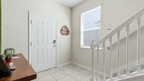 A hallway with a white door, a window with blinds, a wooden desk with a plant, and a white staircase. - Enchanted Palms Villa 7BR w Private Pool (Davenport)