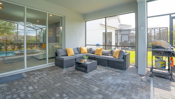 A covered patio with a sectional sofa, a coffee table, and a grill area. - Enchanted Palms Villa 7BR w Private Pool (Davenport)