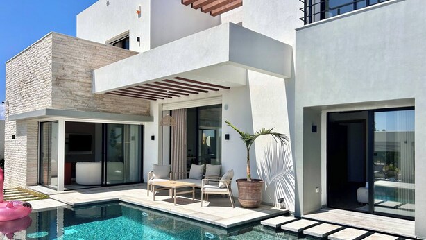 Una casa moderna con piscina, mobiliario exterior y ventanas grandes.