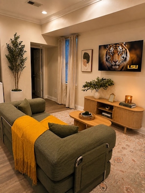 A living room with a sofa, a coffee table, a TV, and a bookshelf. - 2bed 2bath apartment in Baton Rouge 6 min. from LSU fast WiFi, and free parking (Baton Rouge)