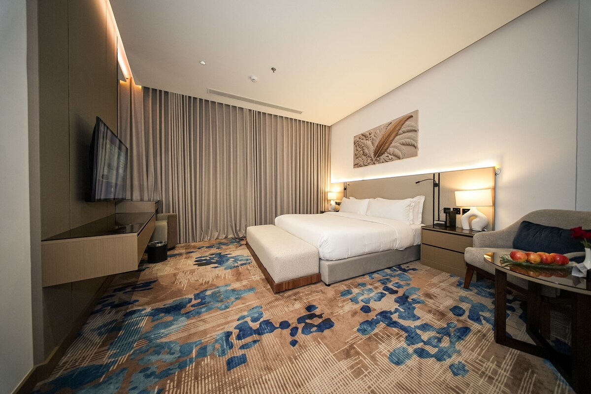 Una habitación de hotel moderna con una cama, mesita de noche, lámpara y un adorno en la pared.