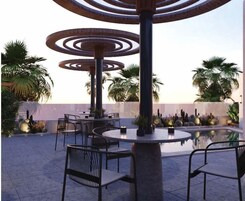 Un espace extérieur aménagé avec des tables et des chaises rondes, entouré de palmiers et de cactus.