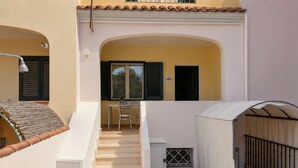 Un escalier menant à un espace extérieur couvert, aménagé avec une table et des chaises, une fenêtre avec des volets et une porte.