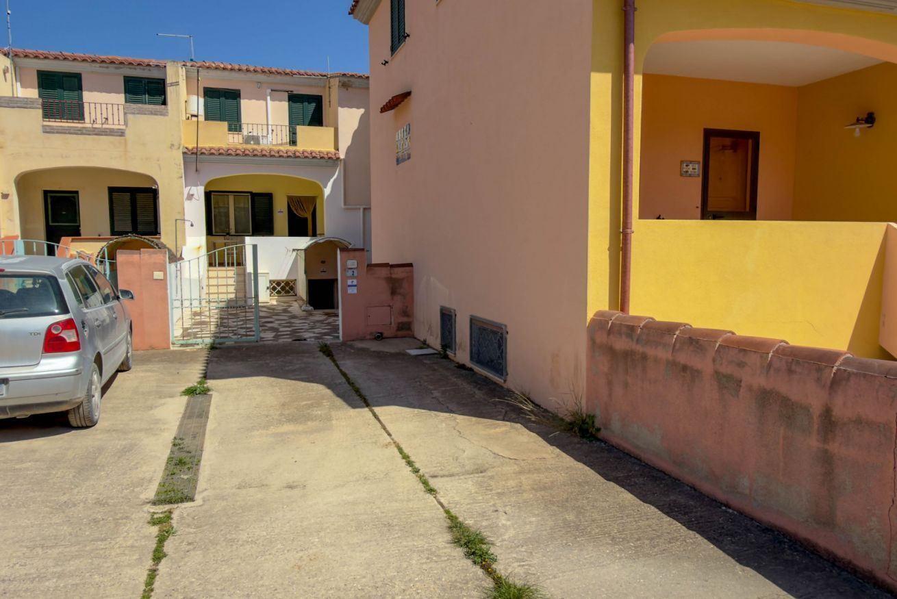 Un estrecho callejón con un coche estacionado, un edificio de fachada amarilla y una escalera que lleva a una entrada.