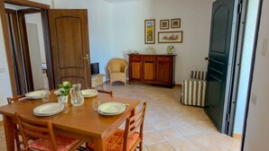 Un coin repas avec une table en bois dressée pour quatre personnes, une chaise en osier, un buffet et une porte donnant sur une autre pièce.