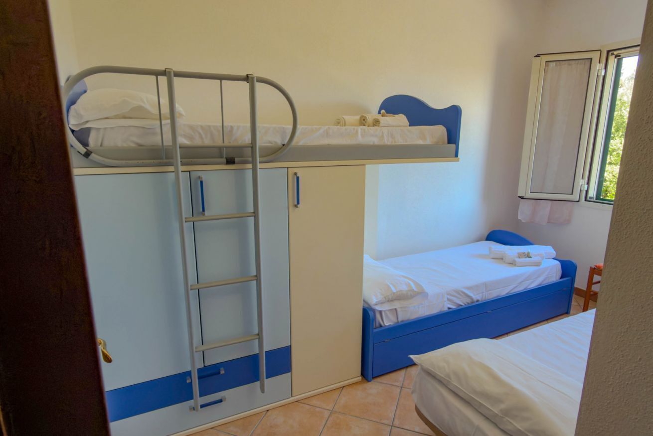 A bunk bed room with a ladder, a lower single bed, and a window with curtains.