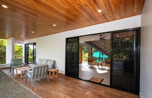 Een modern interieur met een houten plafond, grote schuifdeuren naar een buitenruimte, en een zithoek met een tafel en stoelen.
