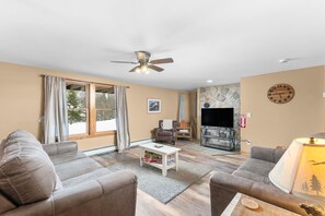 A living room with a sofa, armchair, coffee table, fireplace, TV, and a ceiling fan.