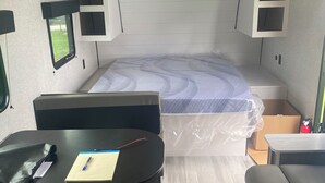 Ein kompaktes Wohnmobil-Interieur mit einem Bett, einem Schreibtisch, einem kleinen Fenster und Stauraumschränken.