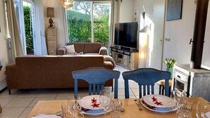 A living room with a sofa, a dining table set with plates and glasses, a television, and a fireplace. - Holiday Home With Spacious Terrace (Sint Maartensvlotbrug)