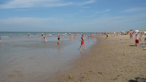 A beach with people walking and playing in the sand, and the ocean in the background. - Holiday Home With Spacious Terrace (Sint Maartensvlotbrug)