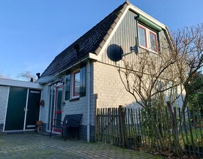 Uma casa com fachada de tijolos, telhado inclinado, cerca de madeira e um banco na parte externa.