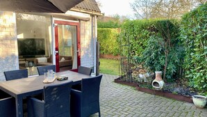 A patio with a table and chairs, a covered area, and a garden with a hedge and plants. - Holiday Home With Spacious Terrace (Sint Maartensvlotbrug)