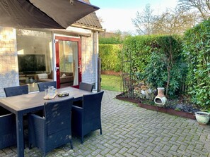 Eine Terrasse mit Tisch und Stühlen, ein überdachter Bereich sowie ein Garten mit Hecke und Pflanzen.