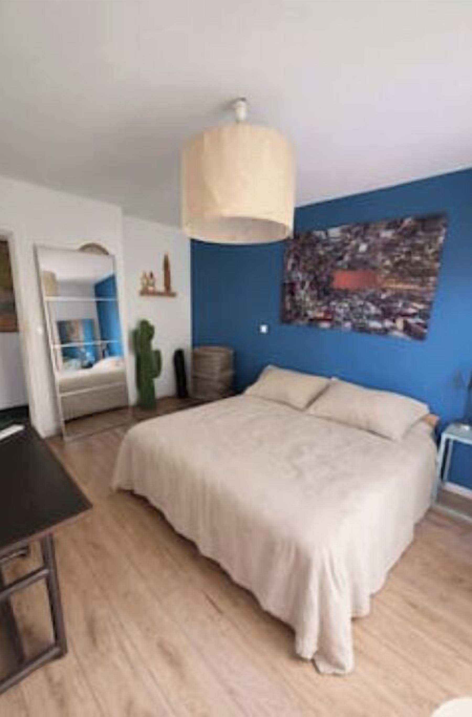 Ein Schlafzimmer mit Bett, Schreibtisch, Stuhl, Pendelleuchte, Wandkunst und einer Kaktee.